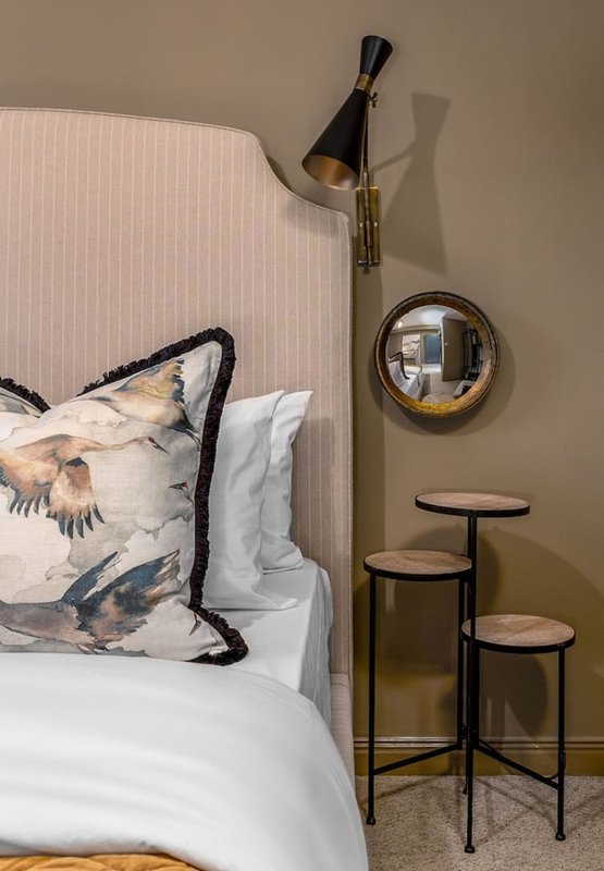 Bedroom corner with upholstered headboard, decorative pillow, wall-mounted lamp and round mirror