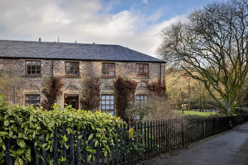 Stone period property with ivy-covered facade, picket fence and bare tree in grounds