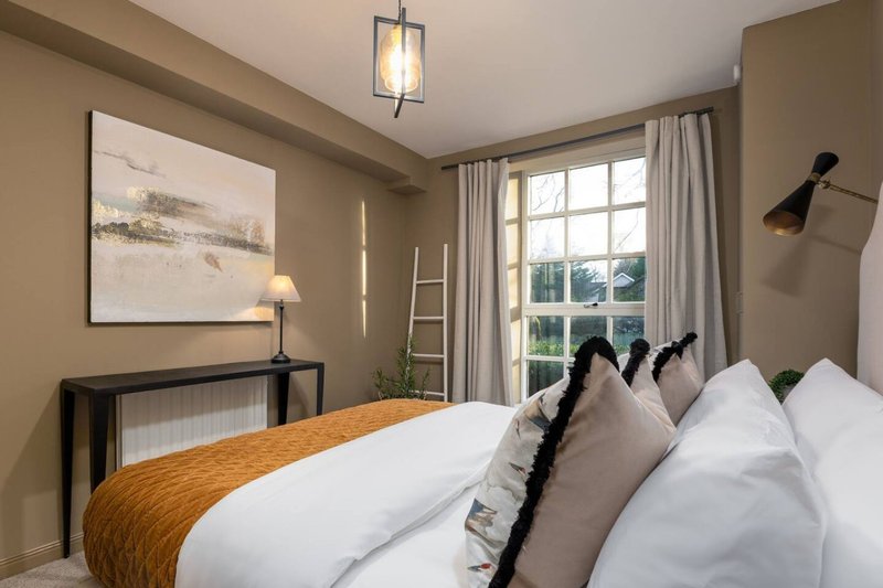 Bedroom with double bed, white bedding, gold throw, multiple pillows and wall-mounted reading lamp