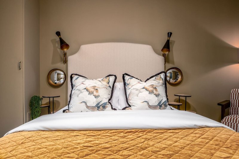 Bedroom with white headboard, yellow quilted bedspread, patterned pillows and wall-mounted lights