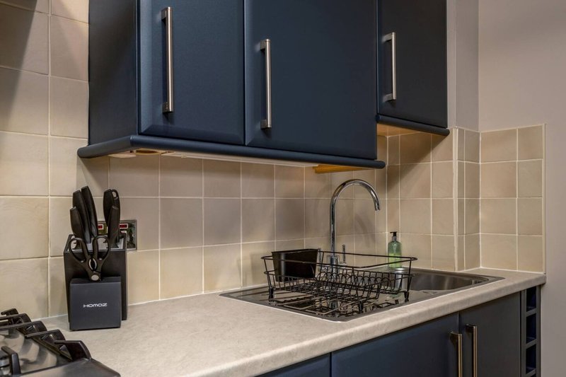 Modern kitchen with dark blue cabinets, white countertop, sink with faucet and dish rack