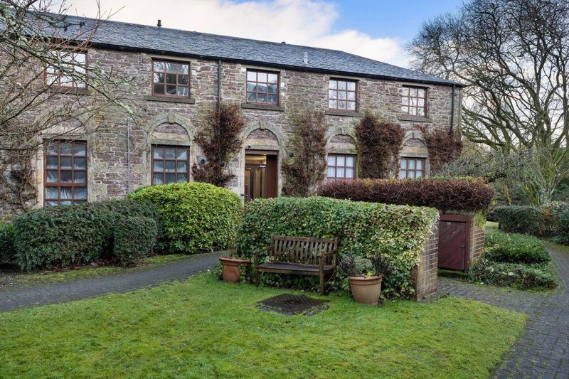 Stone period property with slate roof, multiple windows, front garden with wooden bench and hedging