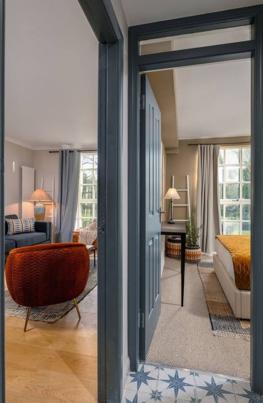 Modern bedroom with double bed, adjacent seating area visible through open doorway with rust-colored chair