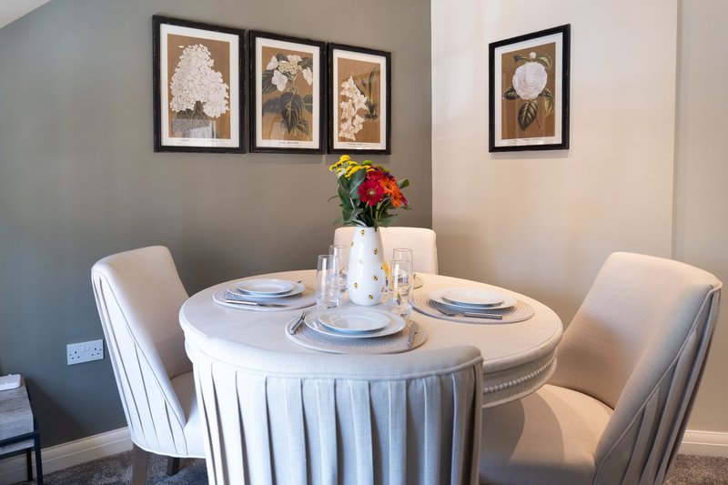 Dining room with round table, white tablecloth, place settings, and framed botanical wall art