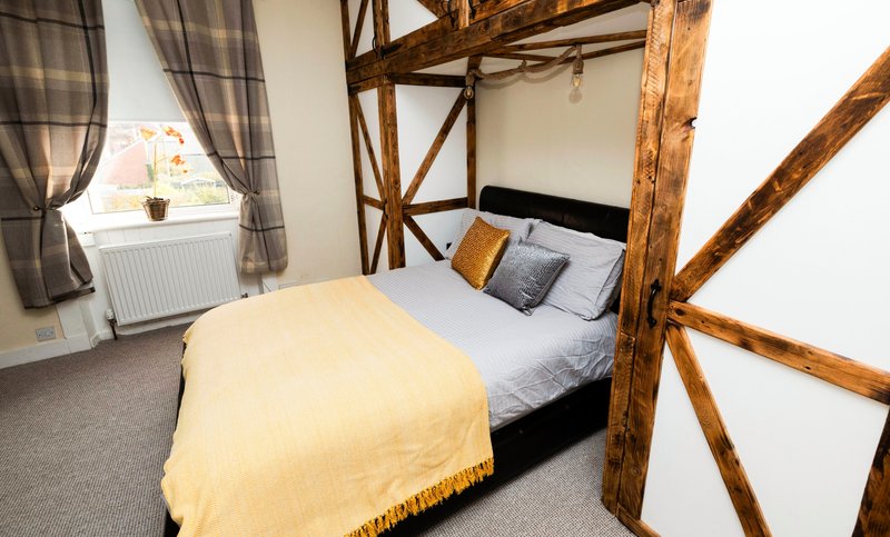 Bedroom with wooden four-poster bed, yellow bedding, plaid curtains and window