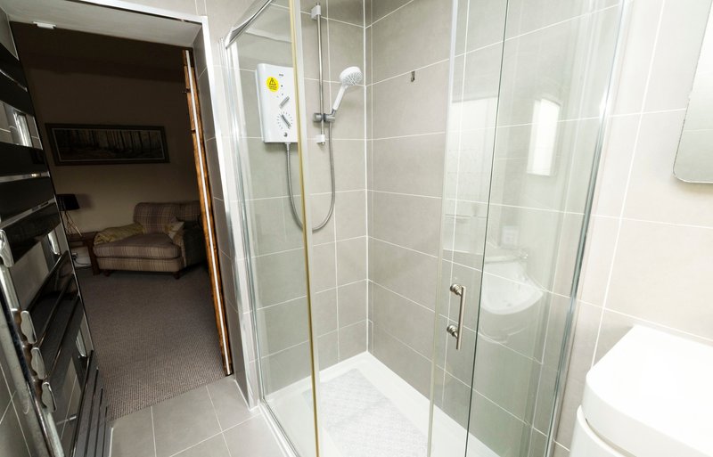 Modern bathroom with glass shower enclosure, toilet, and view into bedroom