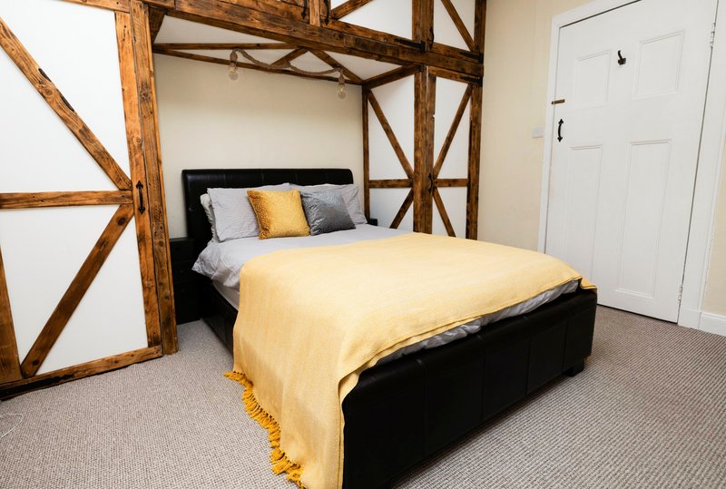 Bedroom with black bed, yellow bedding, decorative pillows, exposed wooden beams and white door