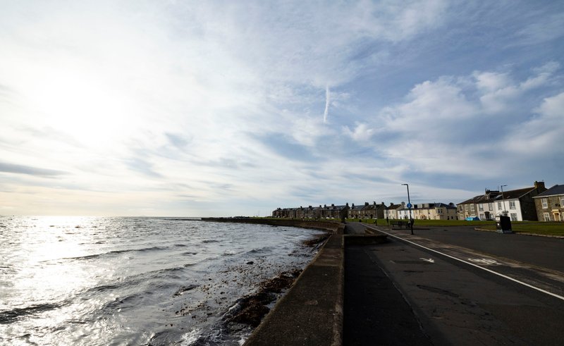 Coastal promenade with beach, sea view, and residential buildings along shoreline