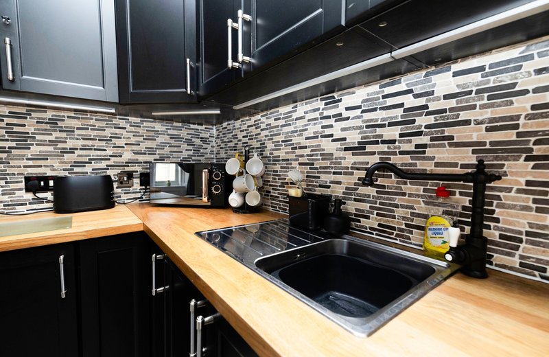 Modern kitchen with black cabinets, wooden countertop, black sink, and tiled backsplash