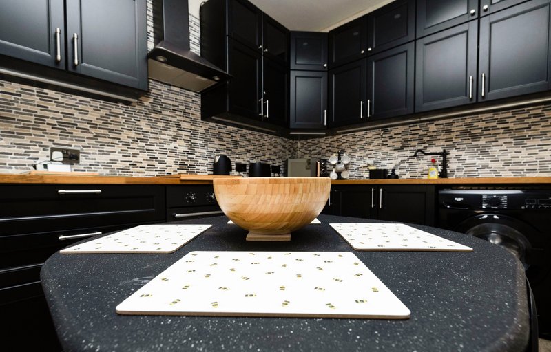 Modern kitchen with black cabinetry, stone backsplash, wooden bowl and countertop styling