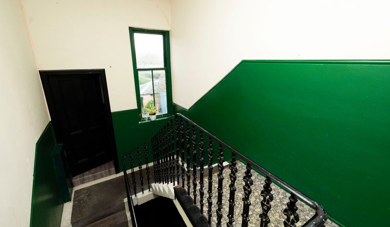 Staircase with green painted walls, wooden spindle railing, and small window
