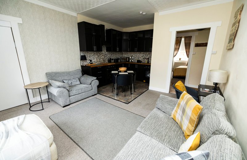 Open-plan living area with grey sofas, black kitchen, dining table and doorways to other rooms
