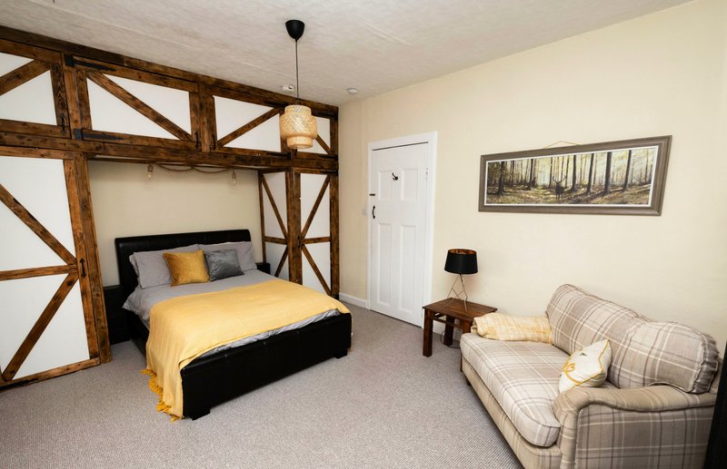Bedroom with double bed, exposed wooden beams, armchair, and framed landscape artwork