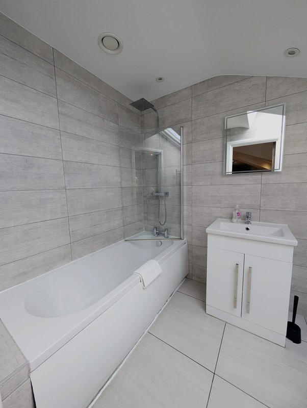 Modern bathroom with white bathtub, gray tile walls, white vanity sink and mirror