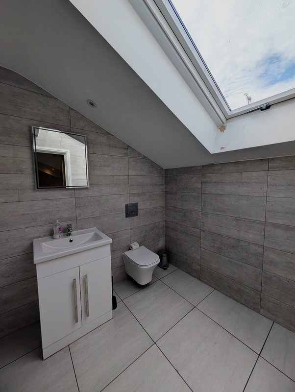 Modern bathroom with white vanity unit, wall-mounted toilet, mirror, and skylight