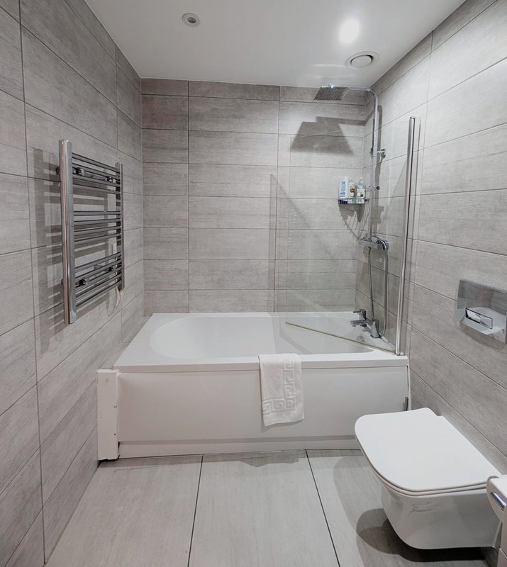 Modern bathroom with white bathtub, glass shower screen, heated towel rail and toilet