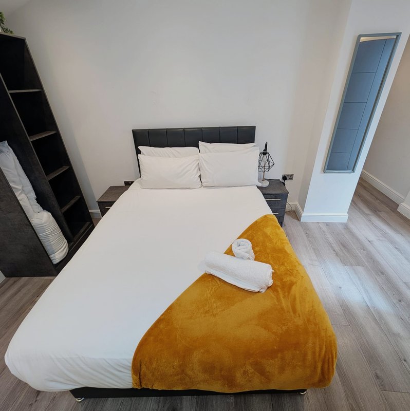 Modern bedroom with double bed, white sheets, golden throw, and black headboard