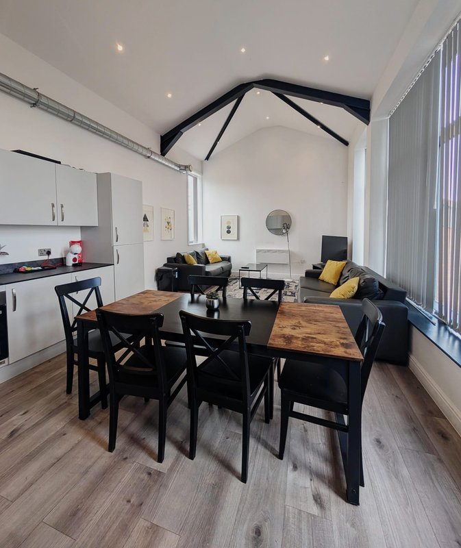 Open-plan living space with dining table, kitchen area, sofa and vaulted ceiling with exposed beams