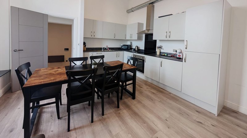 Modern open-plan kitchen and dining area with white cabinetry, black dining table and chairs, wooden flooring