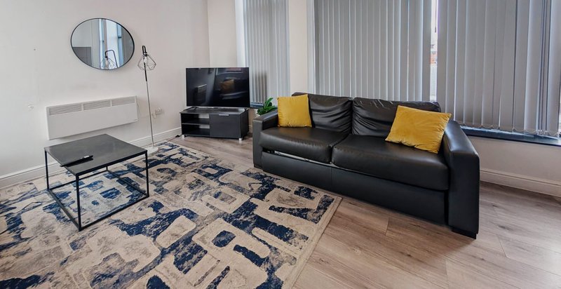 Modern living room with black leather sofa, TV stand, coffee table and patterned rug