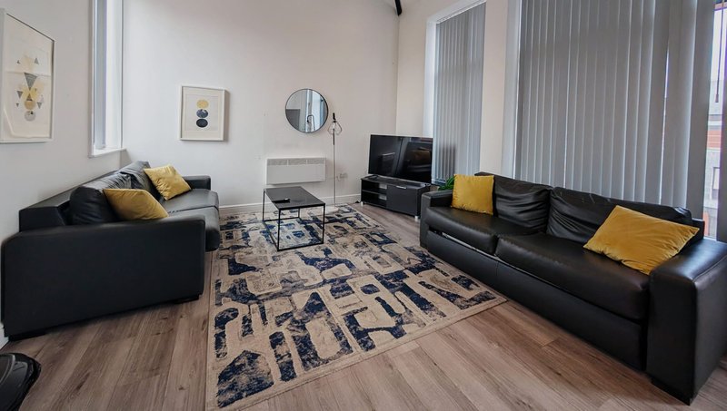 Modern living room with black sofas, yellow cushions, TV, wooden floor and patterned rug