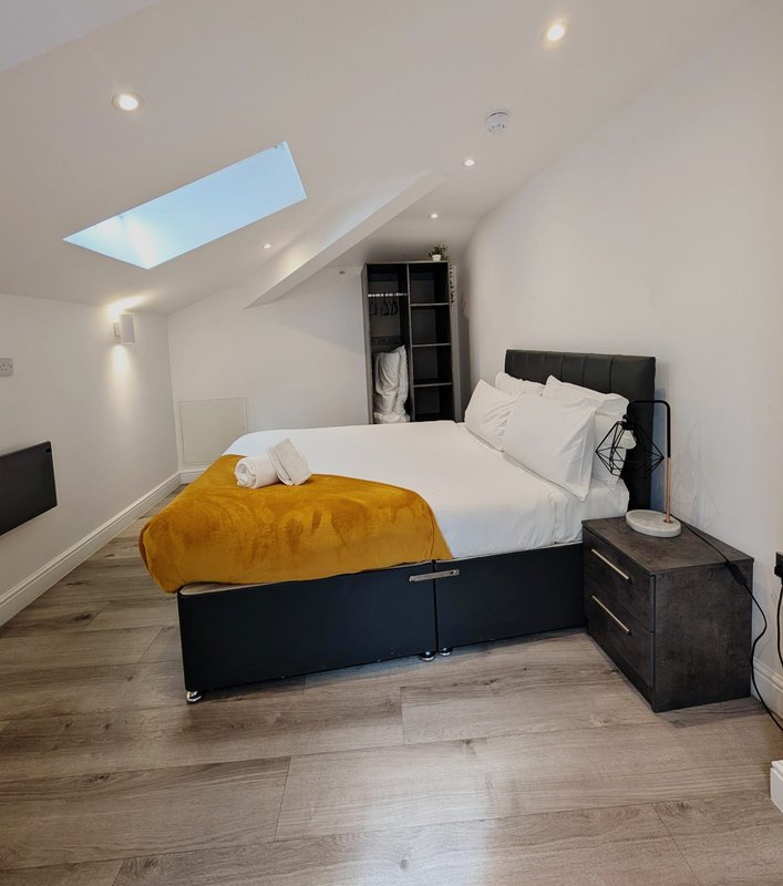 Modern bedroom with double bed, yellow blanket, skylight window, and dark wood flooring