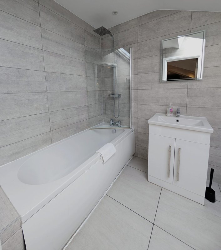 Modern bathroom with white bathtub, glass shower screen, white vanity sink and mirror