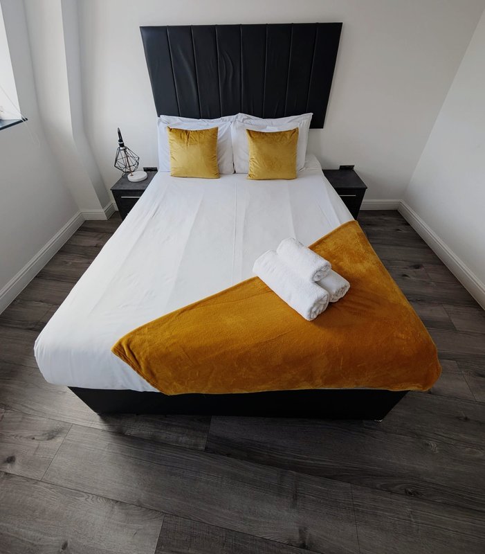 Modern bedroom with black bed frame, white bedding, gold cushions and throw blanket