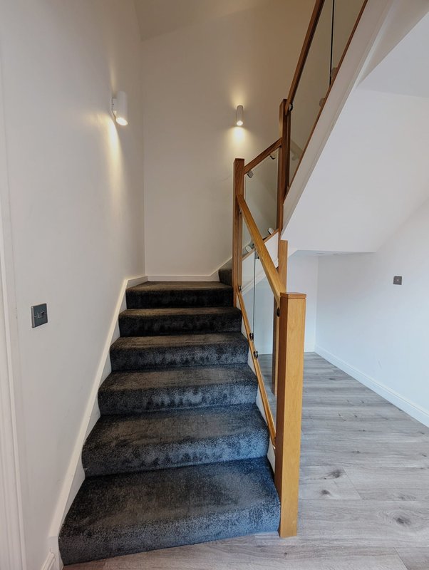 Modern staircase with dark carpet, wooden handrail, and white walls with spotlights