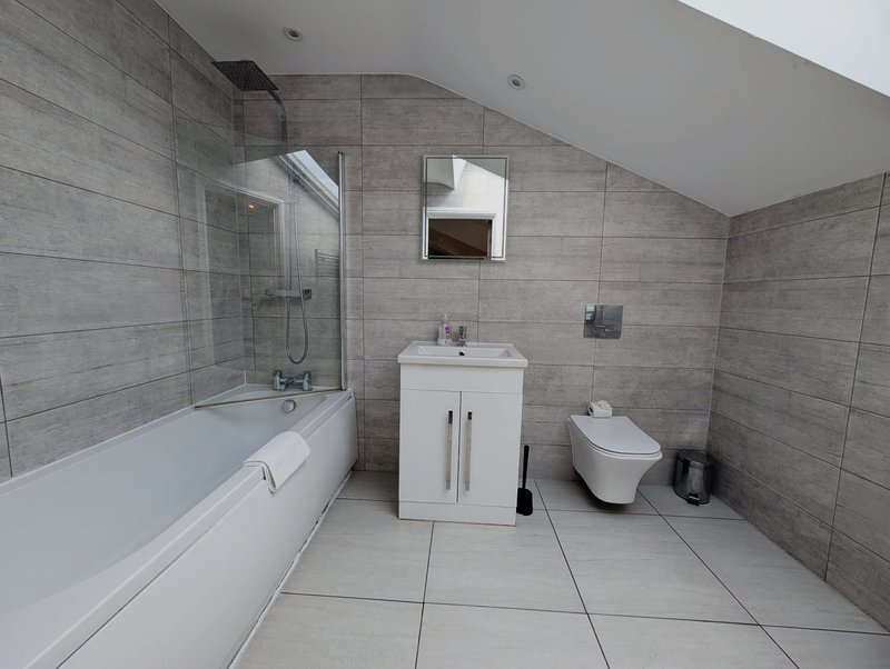Modern bathroom with gray tile walls, white bathtub, wall-mounted sink and toilet