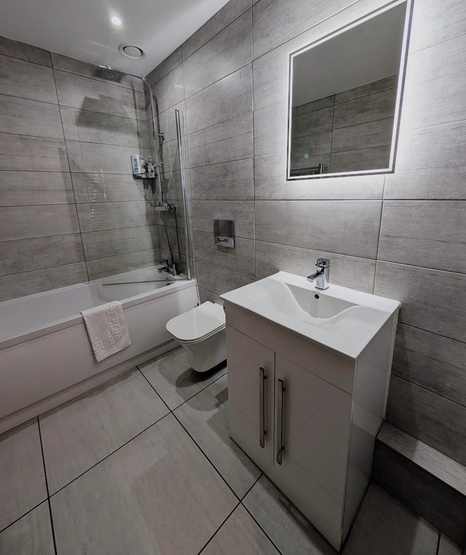 Modern bathroom with grey tile walls, white vanity sink, toilet, and glass shower enclosure