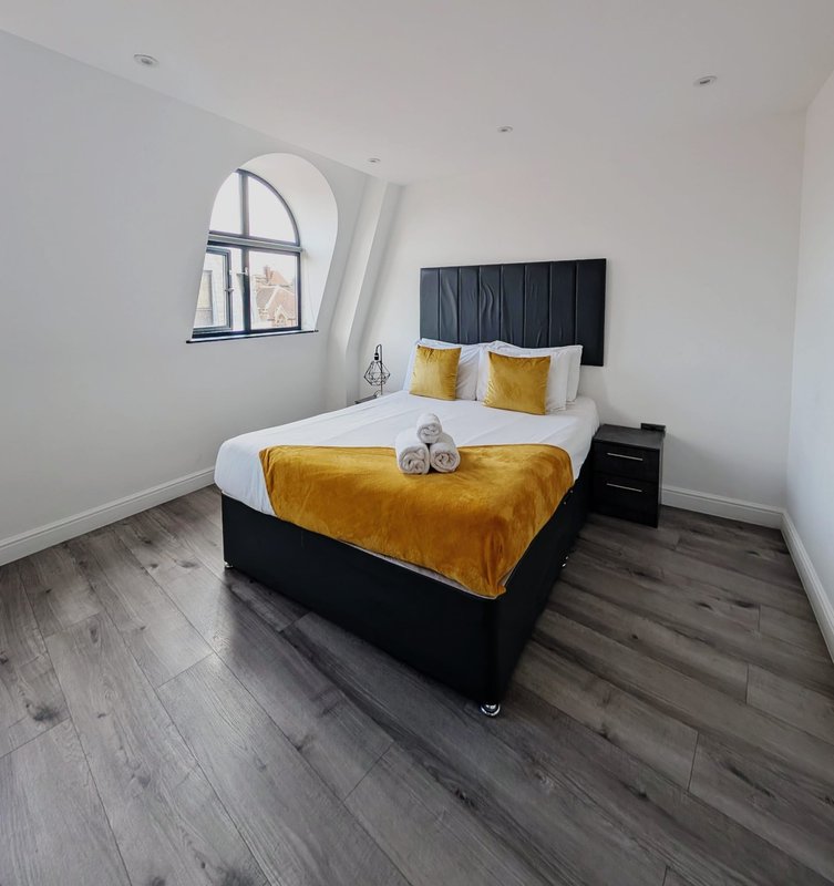 Bright attic bedroom with double bed, yellow bedding, arched window and dark wood flooring