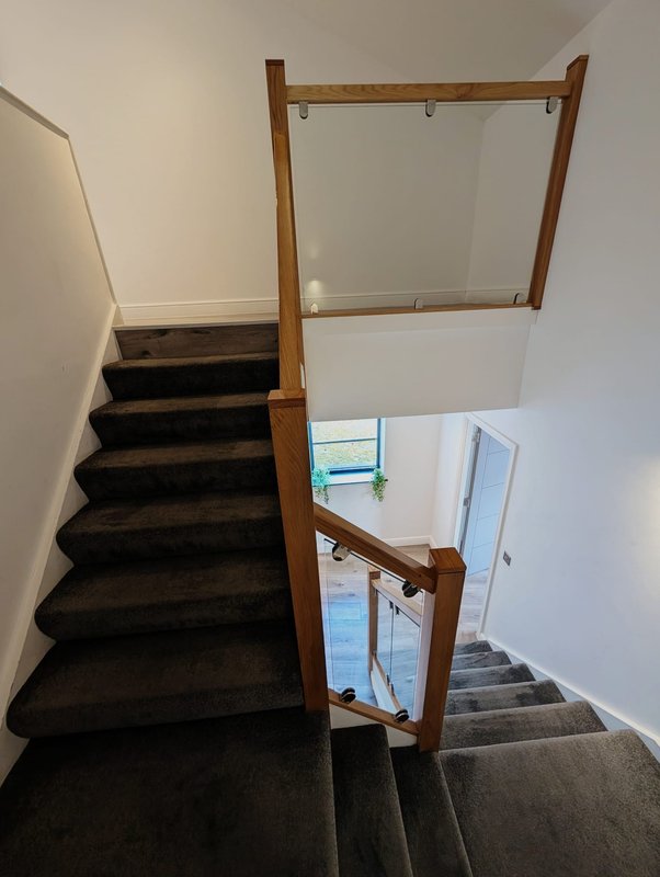 Staircase with dark carpet, wooden handrail and glass panel balustrade, viewed from above