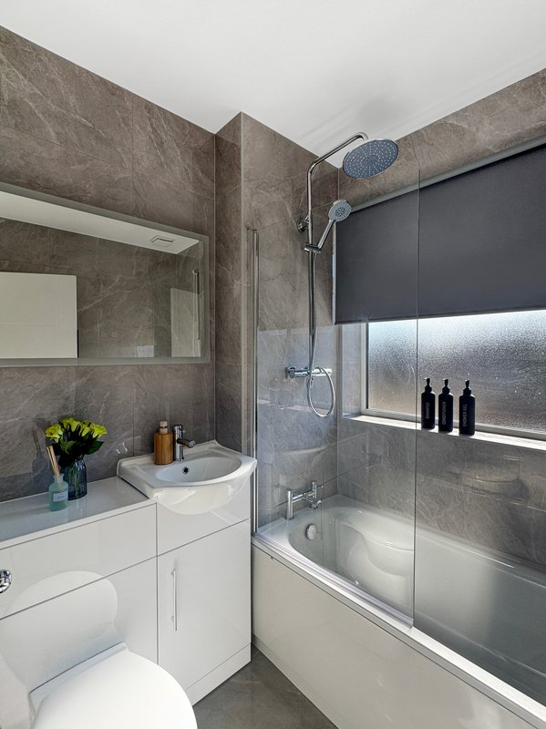 Modern bathroom with grey tile walls, white vanity, toilet, shower enclosure and window