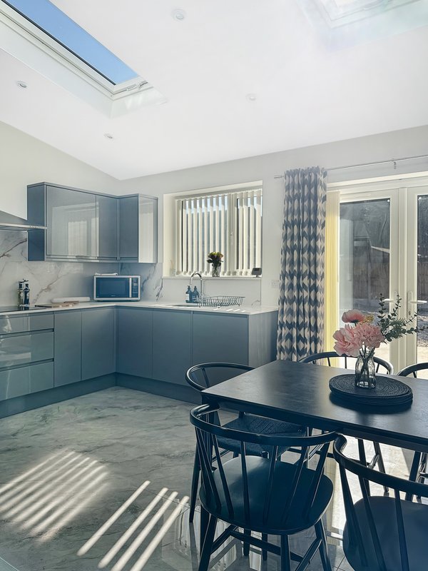 Modern kitchen with blue cabinetry, dining table, skylights and garden door view