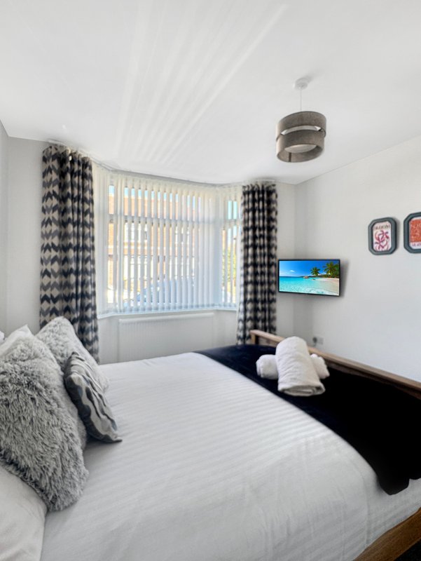 Modern bedroom with double bed, grey textured cushions, patterned curtains, and wall-mounted TV