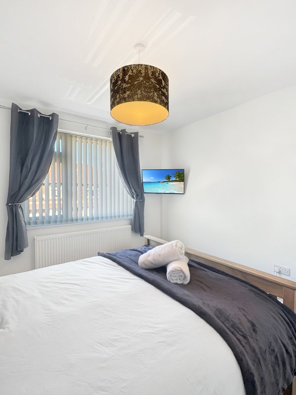 Modern bedroom with double bed, pendant lamp, vertical blinds, dark curtains and wall-mounted TV