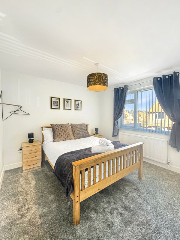 Modern bedroom with wooden bed, bedside table, blue curtains and window overlooking street