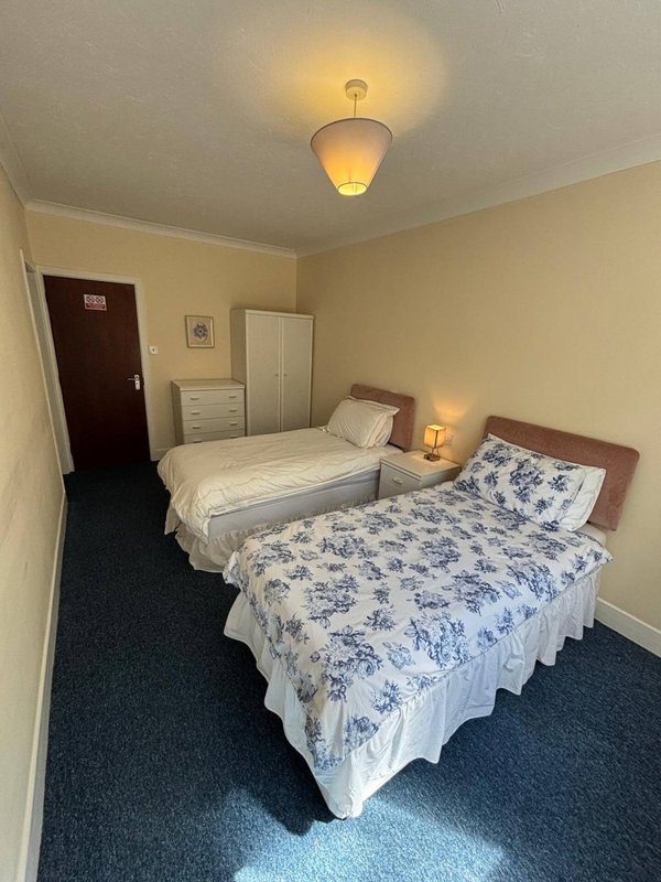 Bedroom with two single beds, bedside lamps, wardrobe and dark carpet flooring