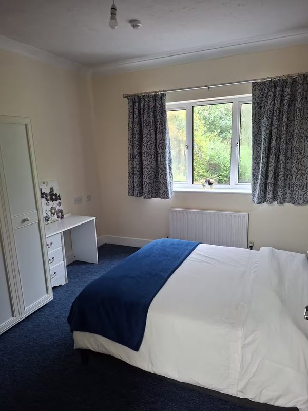 Bright bedroom with double bed, dressing table, window with grey curtains and blue carpet