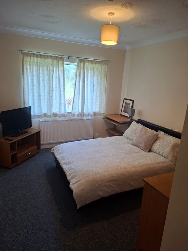 Bedroom with double bed, TV, wooden furniture, and large window with curtains