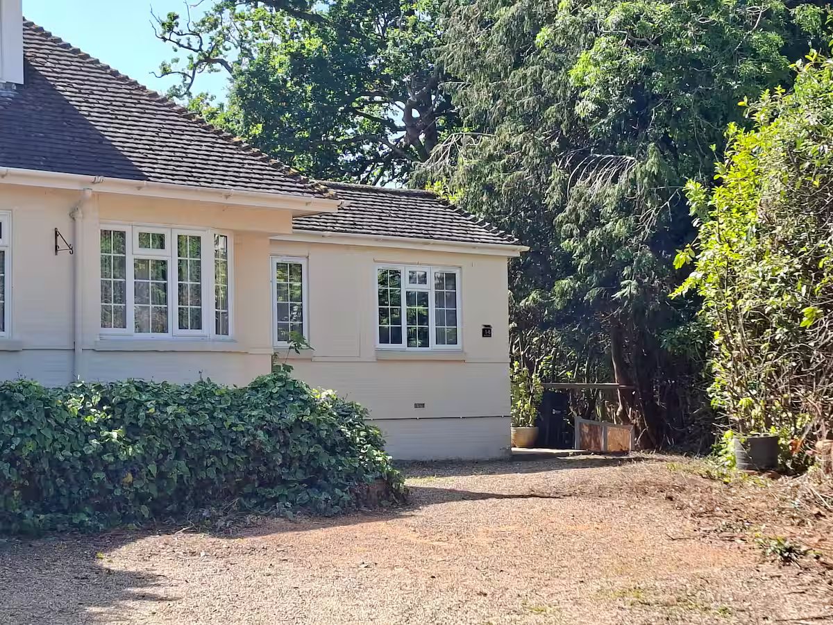 Cream-colored single-story house with garage, driveway, and mature trees