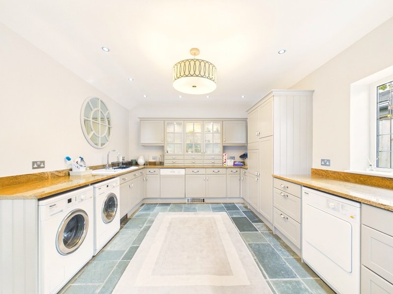 Modern utility room with white cabinetry, wooden counters, two washing machines and tiled floor