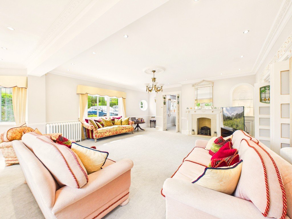 Spacious open-plan living area with cream carpet, pink upholstered sofas, fireplace and windows overlooking garden