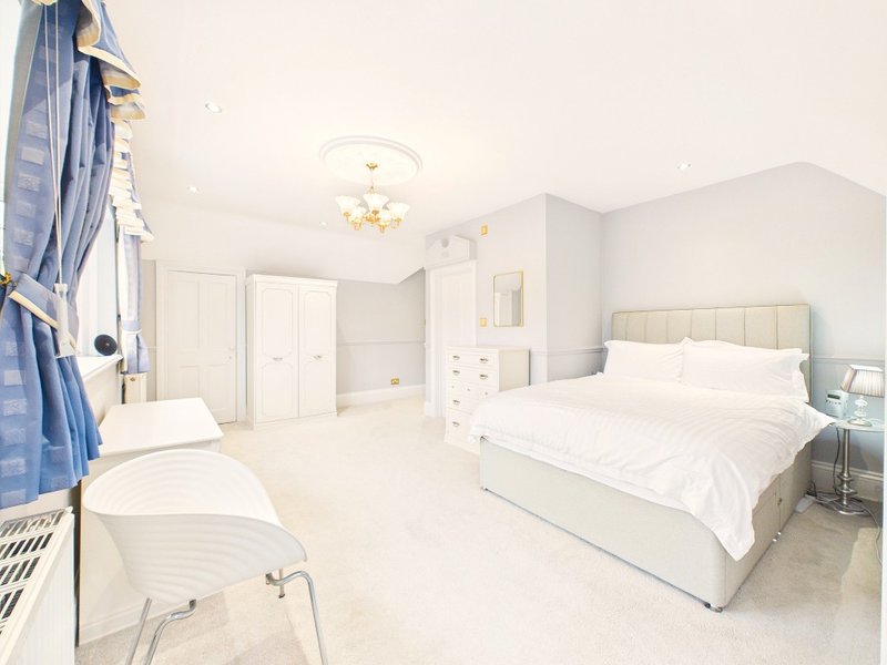 Bright, spacious bedroom with two beds, white furnishings, ceiling light and wardrobes