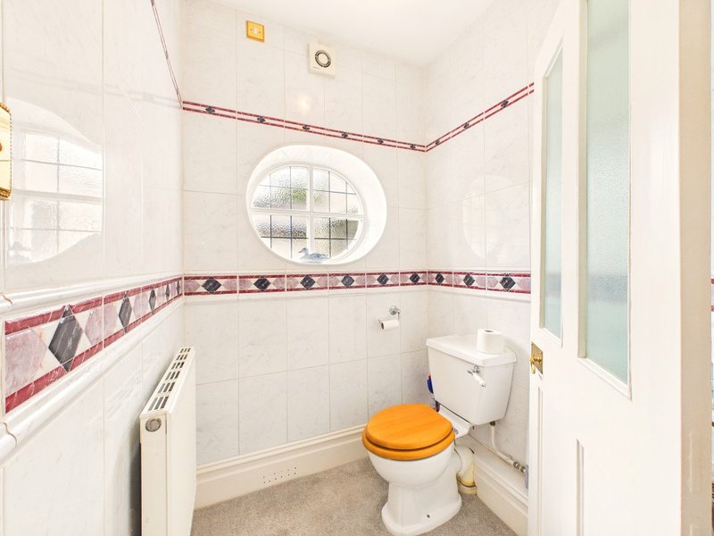 Small bathroom with white tiles, decorative red border, round window, toilet with yellow seat, and radiator