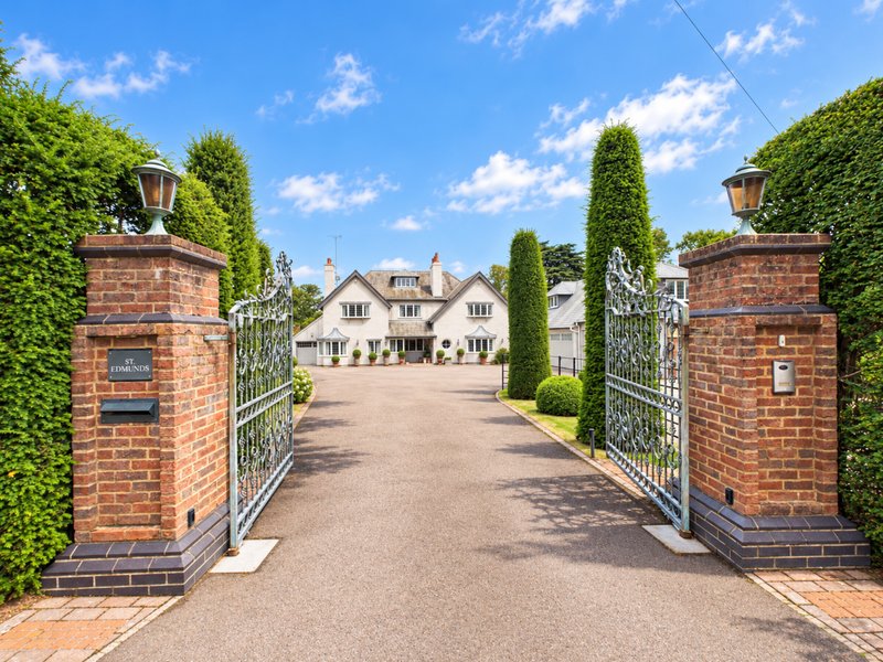 Brick gatehouse pillars with metal gates framing driveway toward stone country house