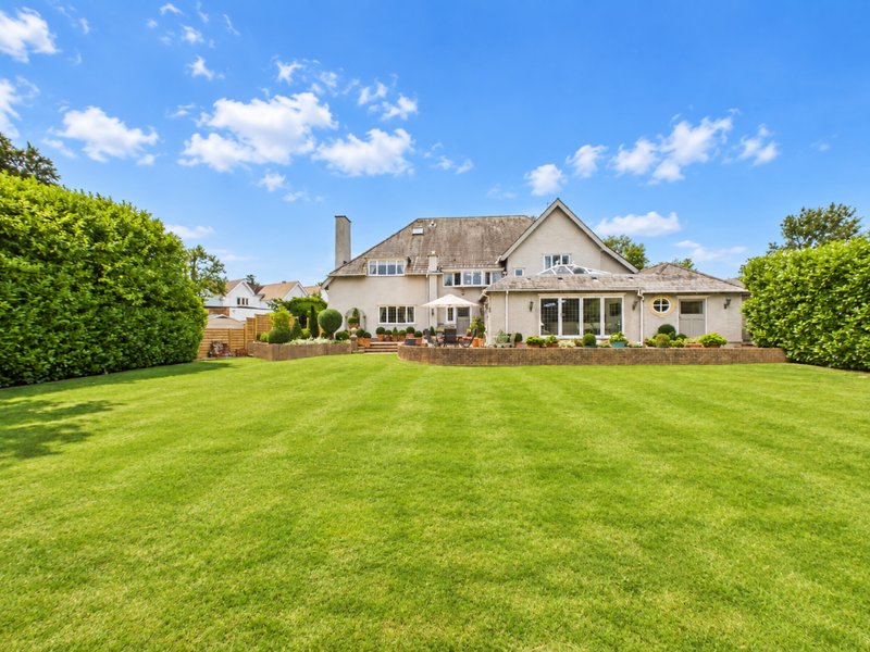 Large stone house with manicured lawn, hedges, and clear blue sky