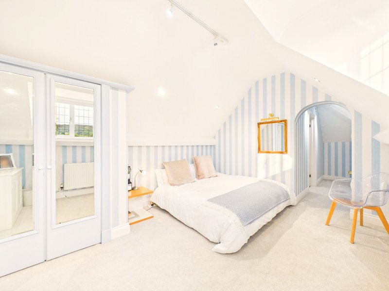 Bright modern bedroom with double bed, striped wallpaper, white doors and orange accents
