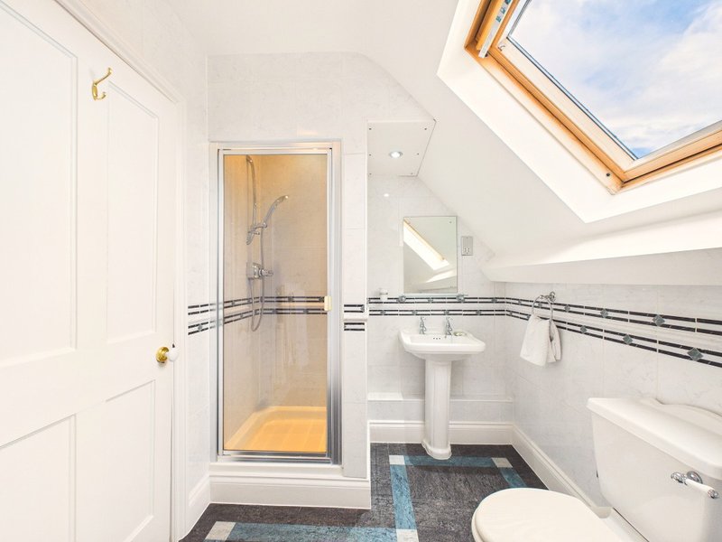 Modern bathroom with shower enclosure, pedestal sink, toilet and skylight window
